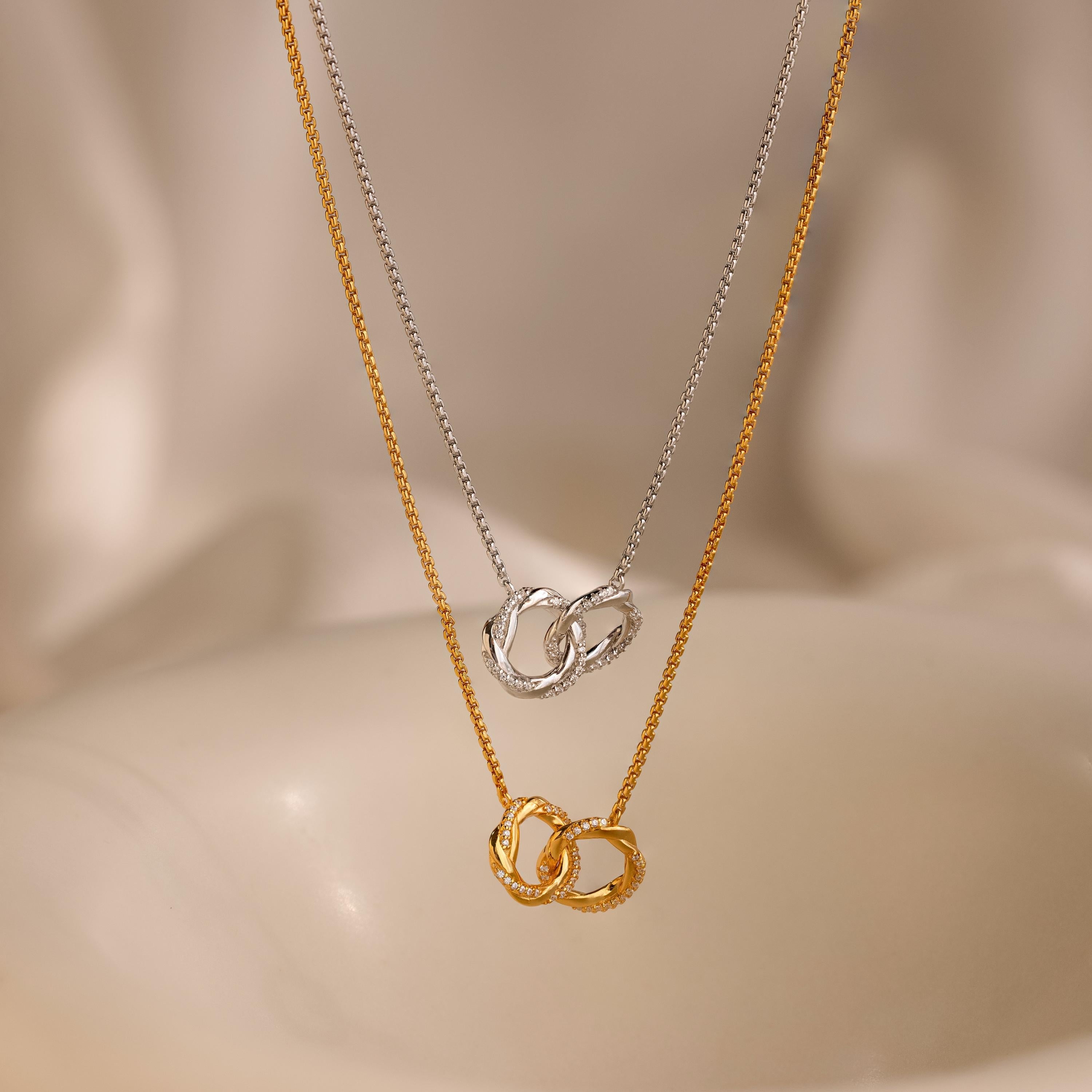 Two interlocking circle charms on a necklace, with one charm paved with diamonds, hanging on a gold-tone chain.